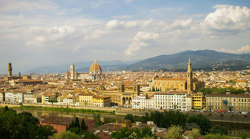 Panorama de la campagne toscane avec collines verdoyantes, champs agricoles et église au centre du paysage.